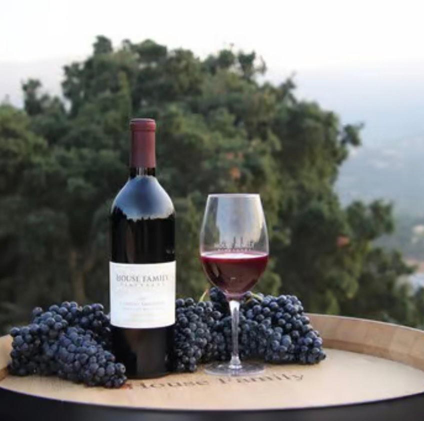 House Family Vineyards wine bottle and glass with grapes on a barrel